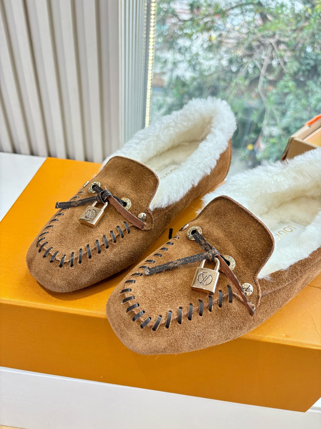 Brown suede shearling loafers with lace-up ties and stitched trim, two shoes on box