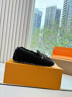 Black suede loafers on tan box, side view with silver-tone lace detail.