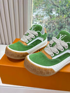 Two green suede sneakers with white laces and tan rubber soles on orange box