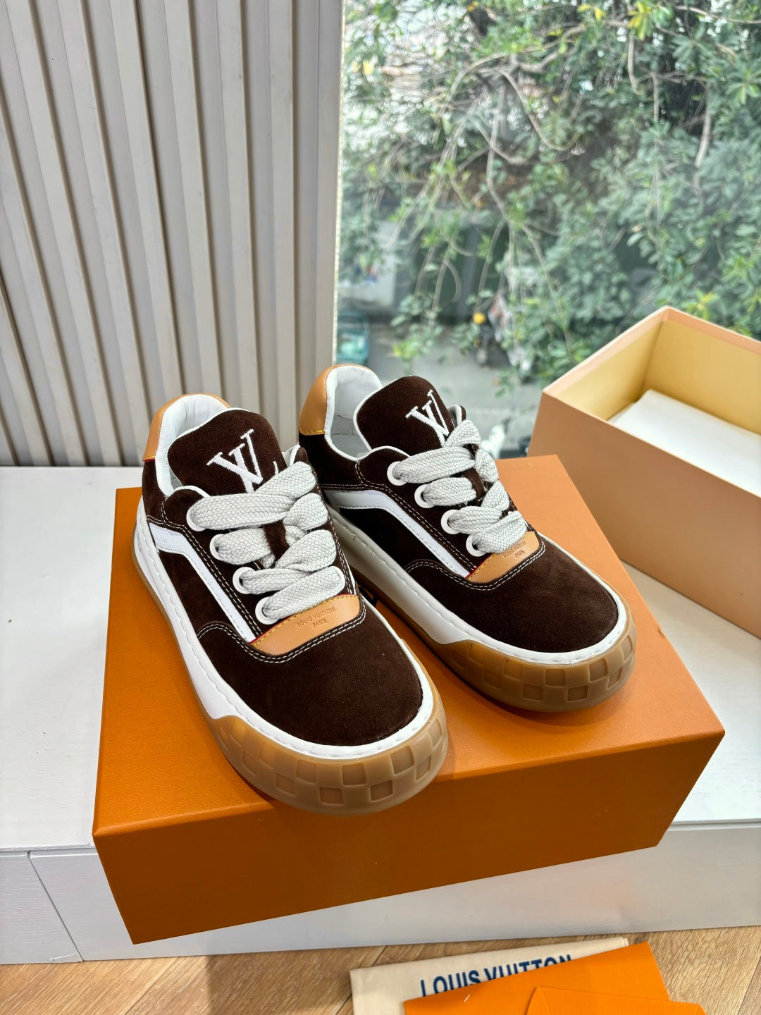 Brown suede sneakers with white laces, LV tongue logo, on orange presentation box.