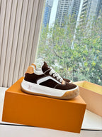 Brown suede low-top sneaker with white sole and LV logo, resting on orange box.