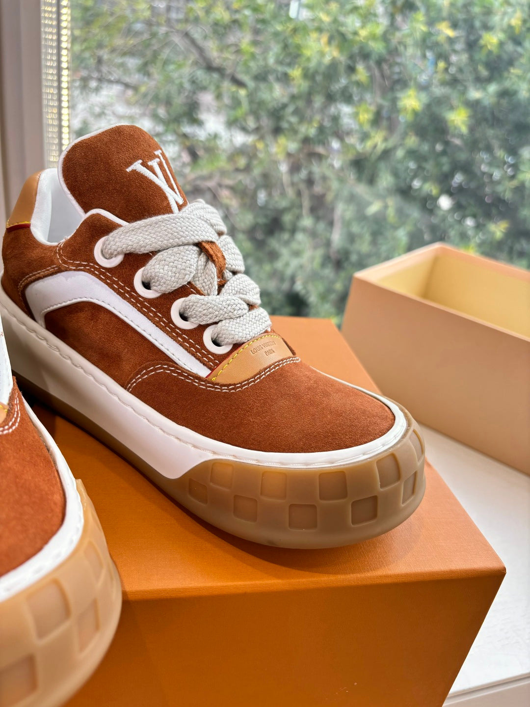 Close-up of brown suede sneaker with white laces and side LV emblem on box.