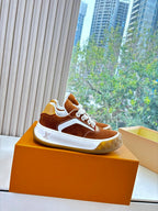 Brown suede sneakers with white trim and laces on orange display box.