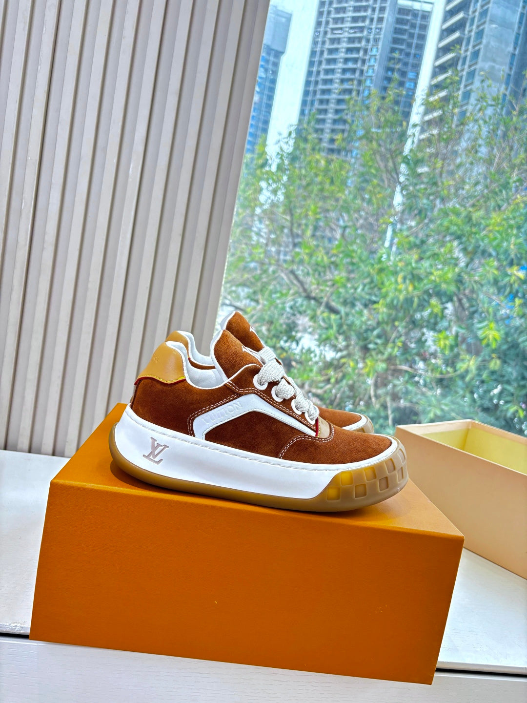 Brown suede sneakers with white trim and laces on orange display box.
