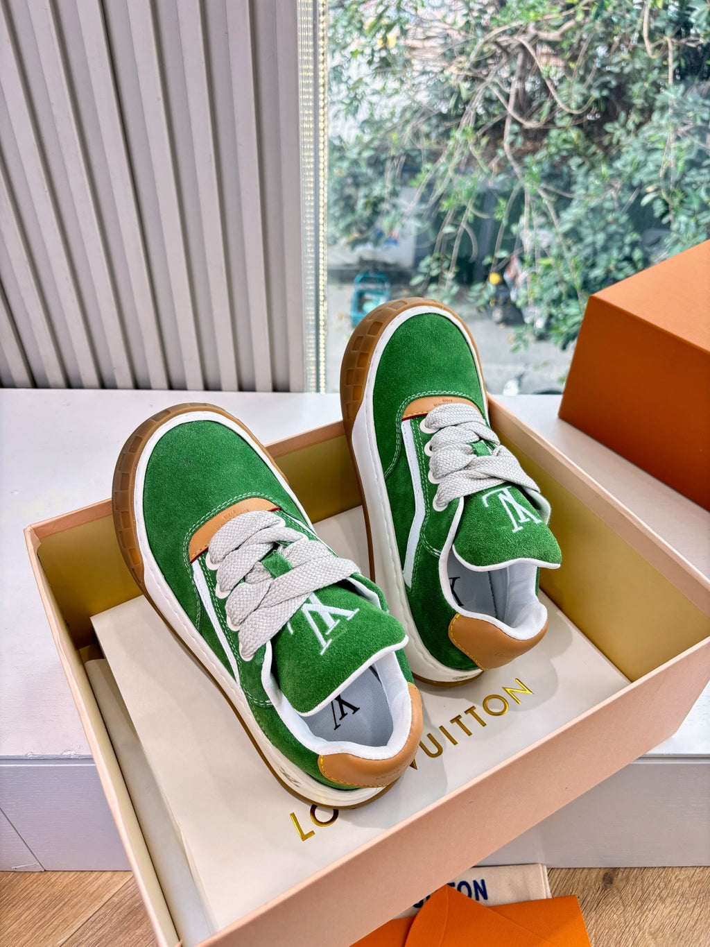 Pair of green suede sneakers with white laces and tan rubber soles in open box
