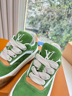 Close-up of green suede sneakers with white laces, LV emblem on side, in box