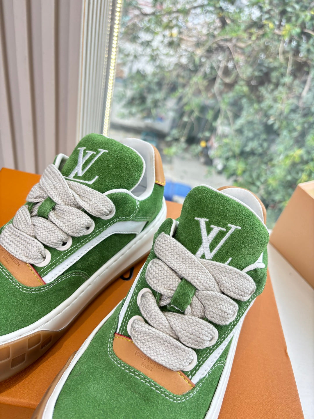 Close-up of green suede sneakers with white laces, LV emblem on side, in box