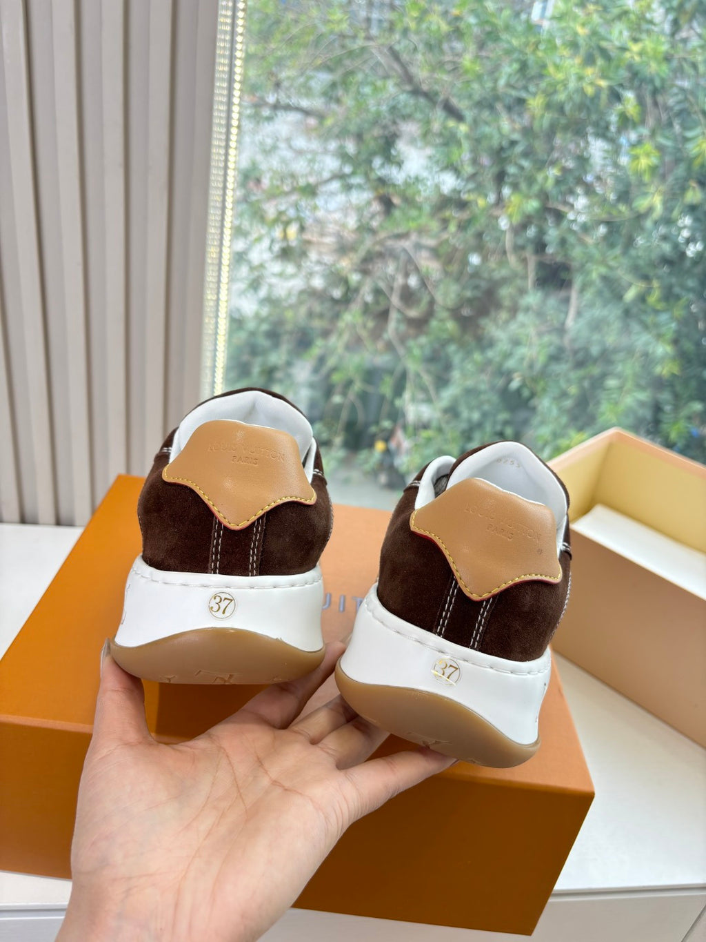Brown suede sneakers heel view with white soles and LV branding detail, in box.