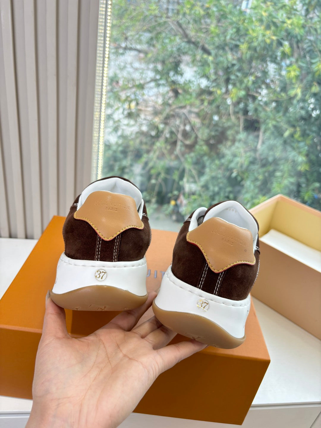 Brown suede sneakers heel view with white soles and LV branding detail, in box.