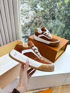Brown suede sneakers with white laces and chunky sole, held near open box.