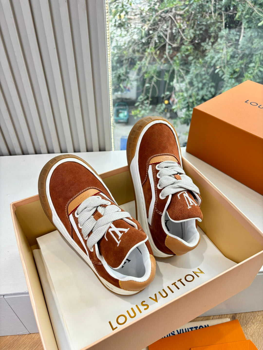 Brown suede sneakers with white laces and LV logo, front angle in box.