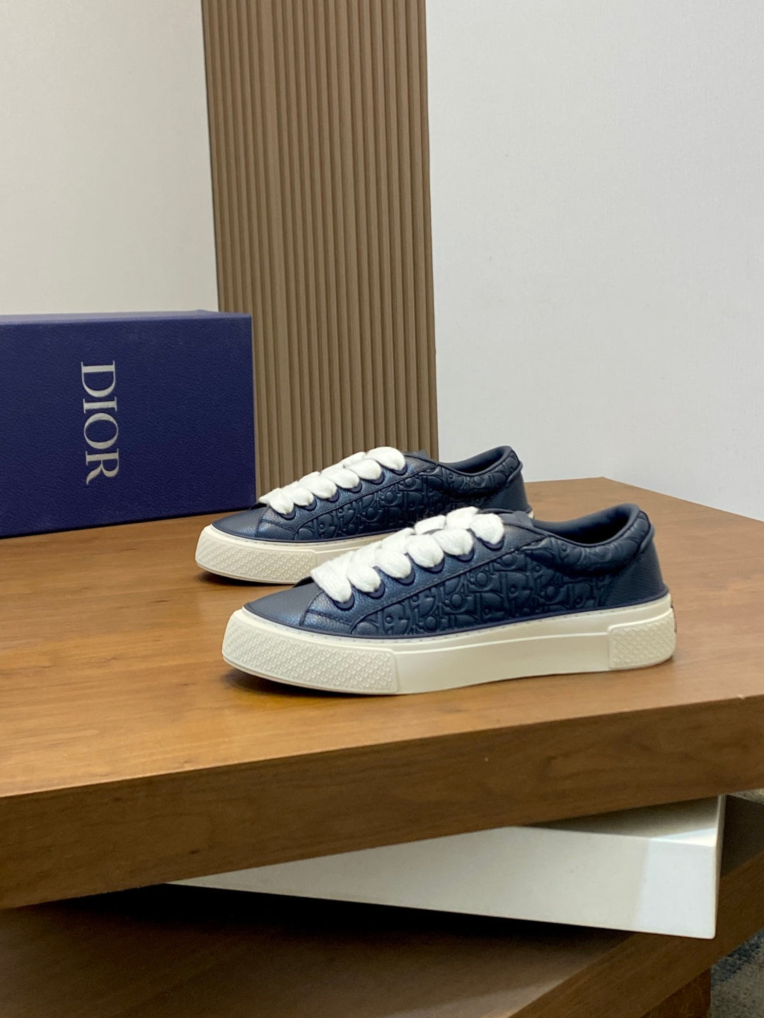 Navy low-top Dior sneakers with white laces on a wooden display shelf