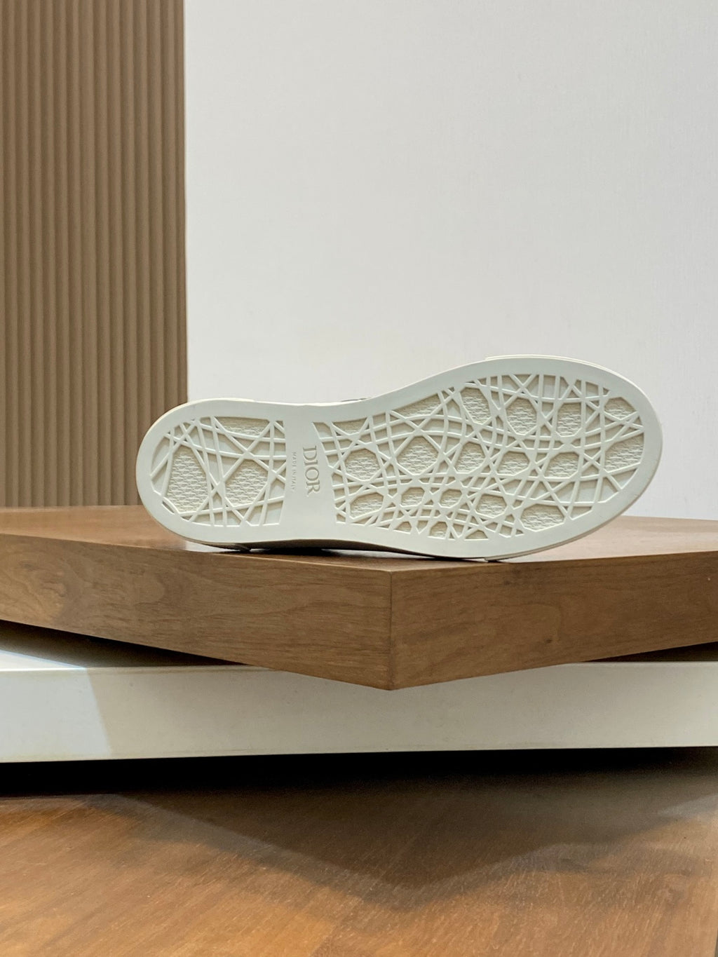 Navy sneaker outsole with white patterned tread displayed on a wooden shelf