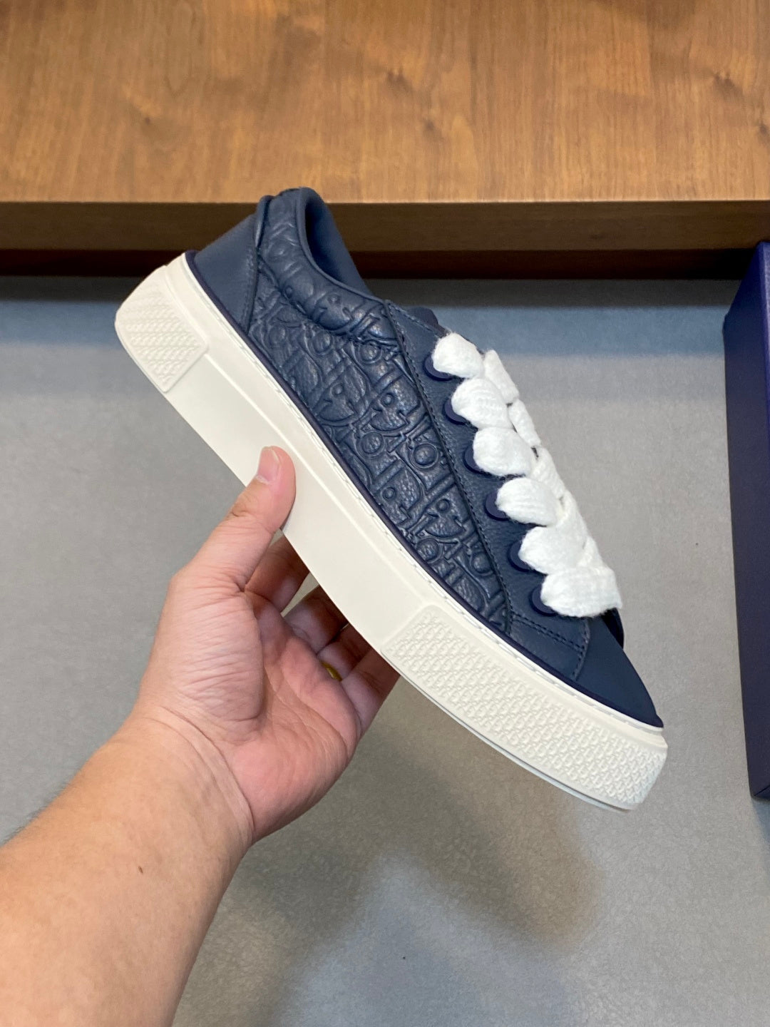Navy low-top sneaker with white laces held in a hand, textured upper