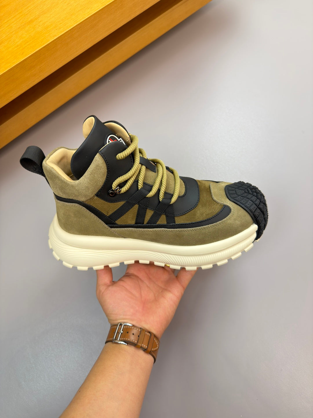 Moncler sneakers profile view on hand: olive suede, black panels, white cushioned sole