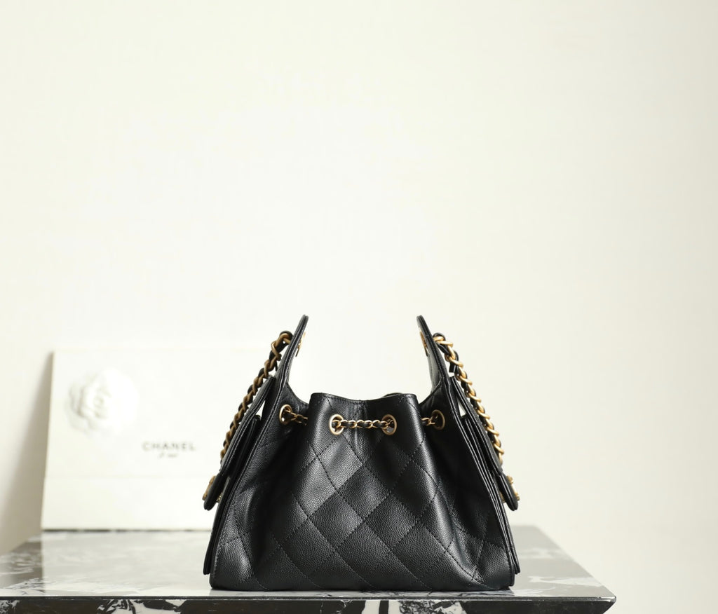 Chanel black leather bucket bag with quilted texture, gold chain shoulder strap, and pouch top
