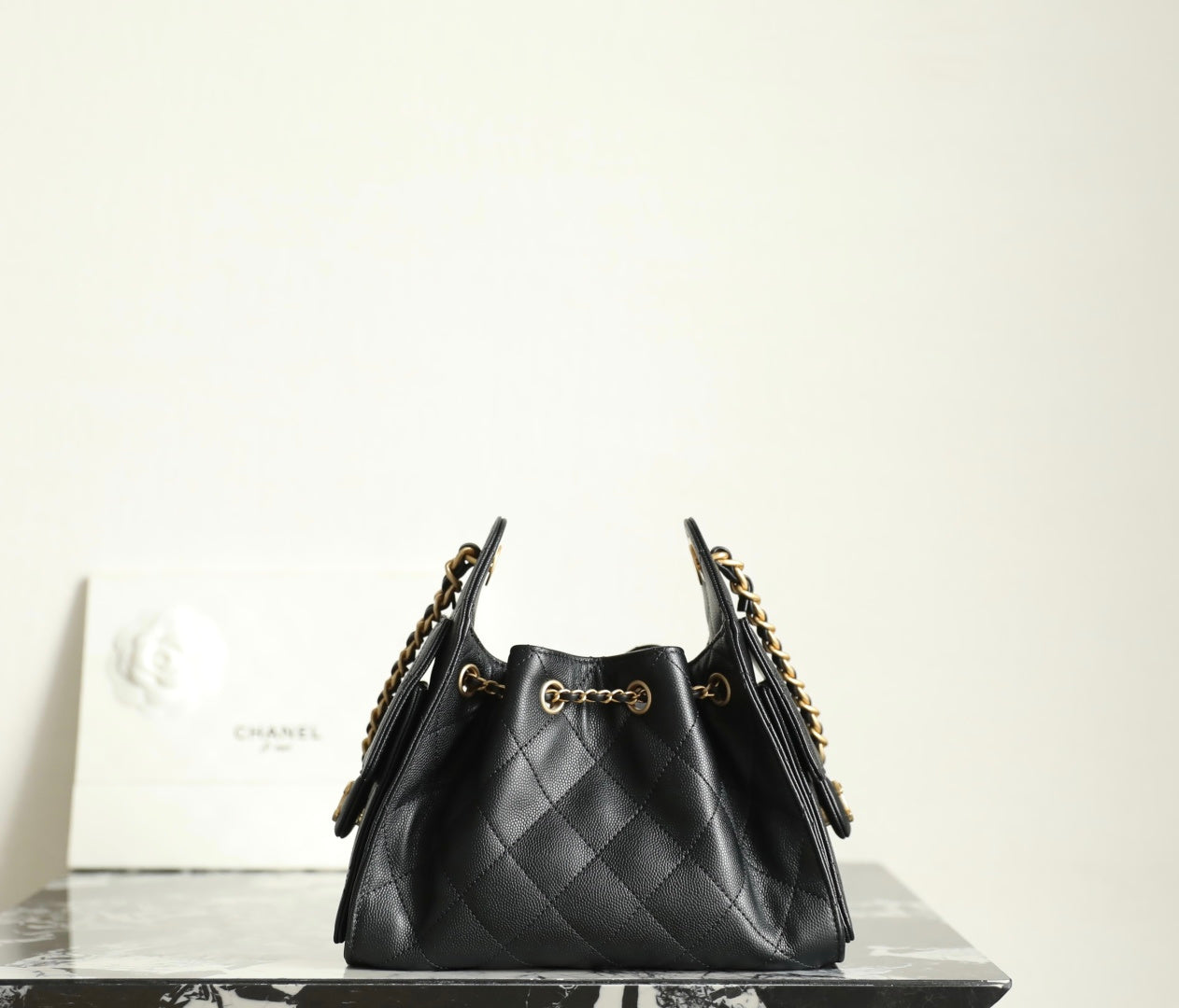 Chanel black leather bucket bag with quilted texture, gold chain shoulder strap, and pouch top
