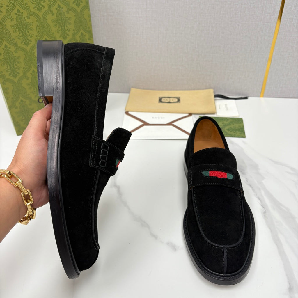 Gucci unisex black suede loafers shown on hand, side buckle detail and stripe.