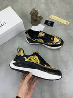 Versace low-top sneakers, black with gold accents and white sole, one shoe held in hand