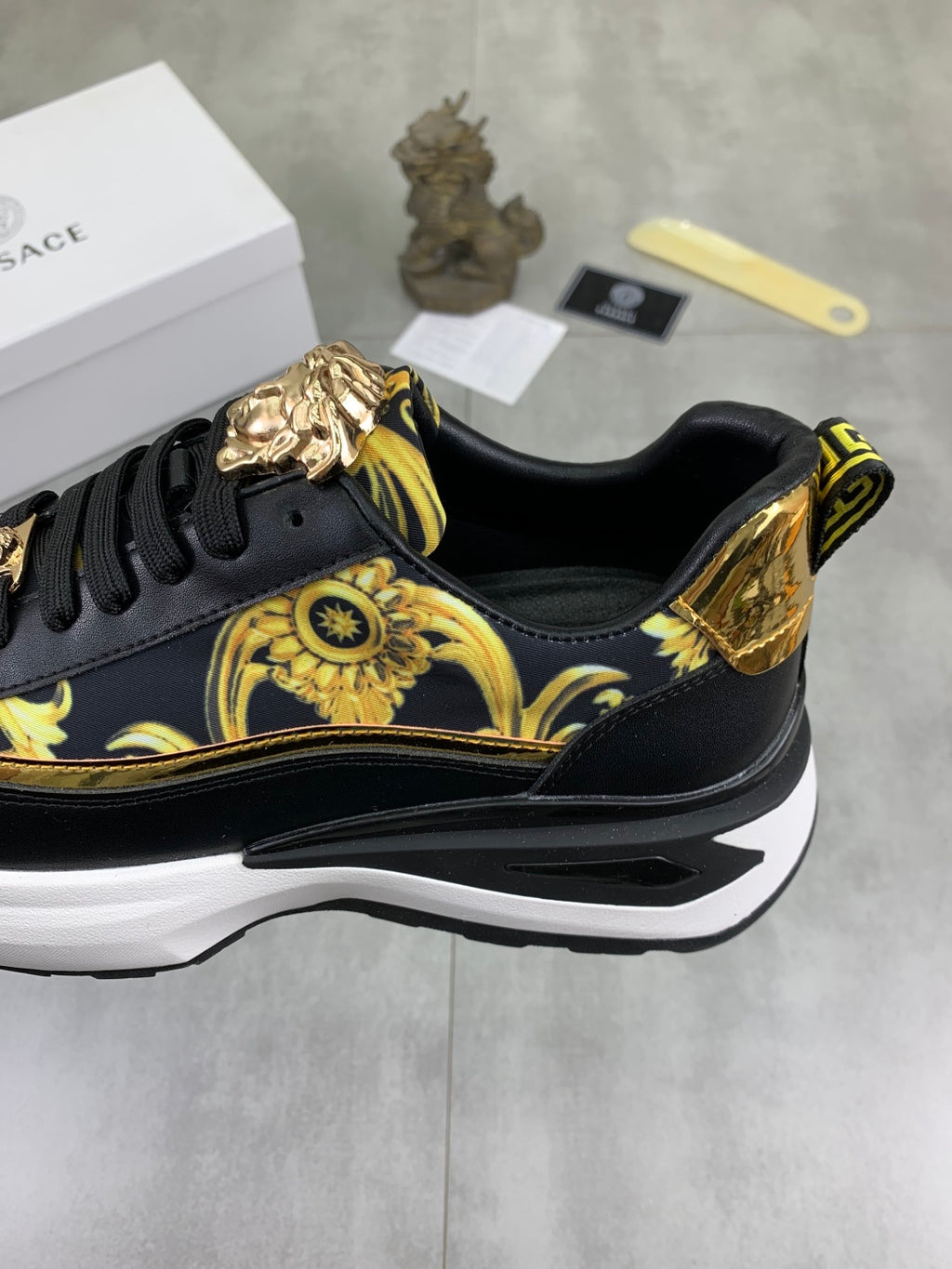 Versace low-top sneaker close-up: black and gold patterned upper with sculpted emblem on side