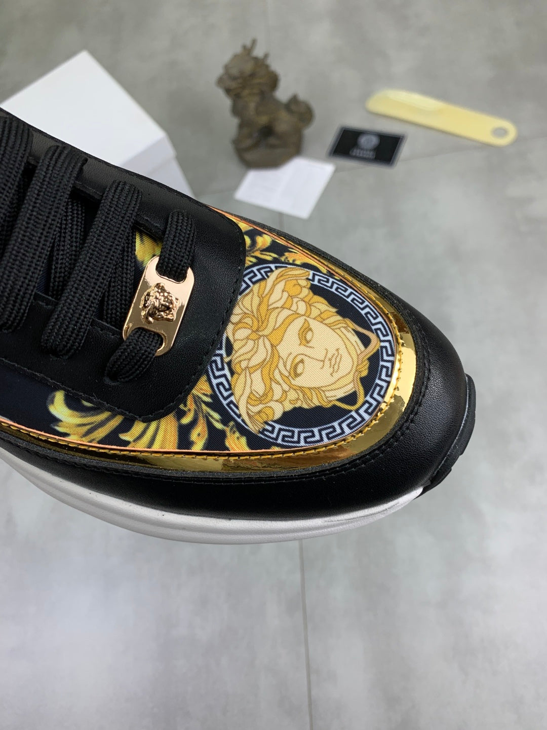 Versace low-top sneaker detail: black upper with gold baroque emblem and blue-gold trim