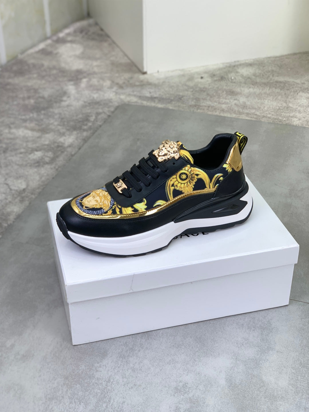 Versace low-top sneakers on white box, black leather-look with gold crest accents and white sole