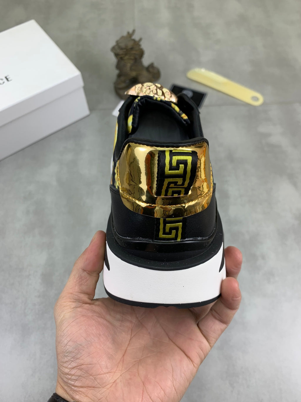Versace low-top sneaker heel view, black upper with gold logo panel and white midsole