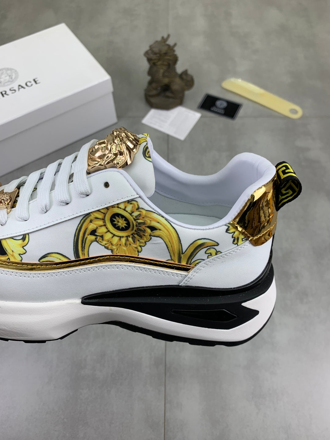 Versace white sneakers with gold medallion detailing and oversized black sole edge