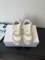 Cream lace-up sneakers with padded collar, stitched panels, and flat sole on box
