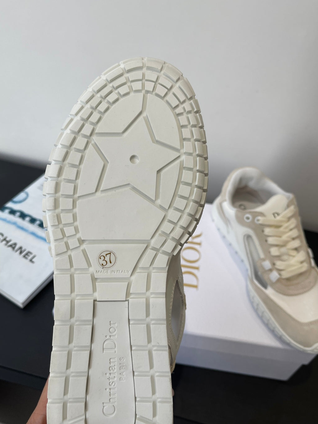 Shoe outsole with tread pattern and Dior mark, shown with one cream sneaker