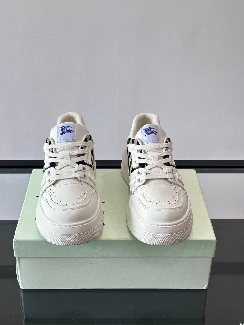 White lace-up sneakers pair on box, black check side panels and blue logo patch