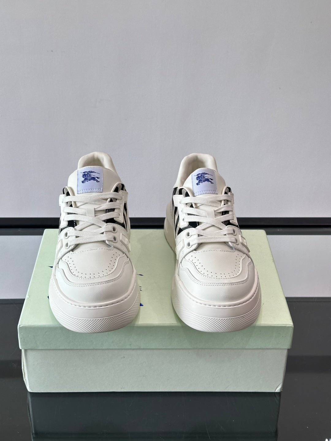 White lace-up sneakers pair on box, black check side panels and blue logo patch