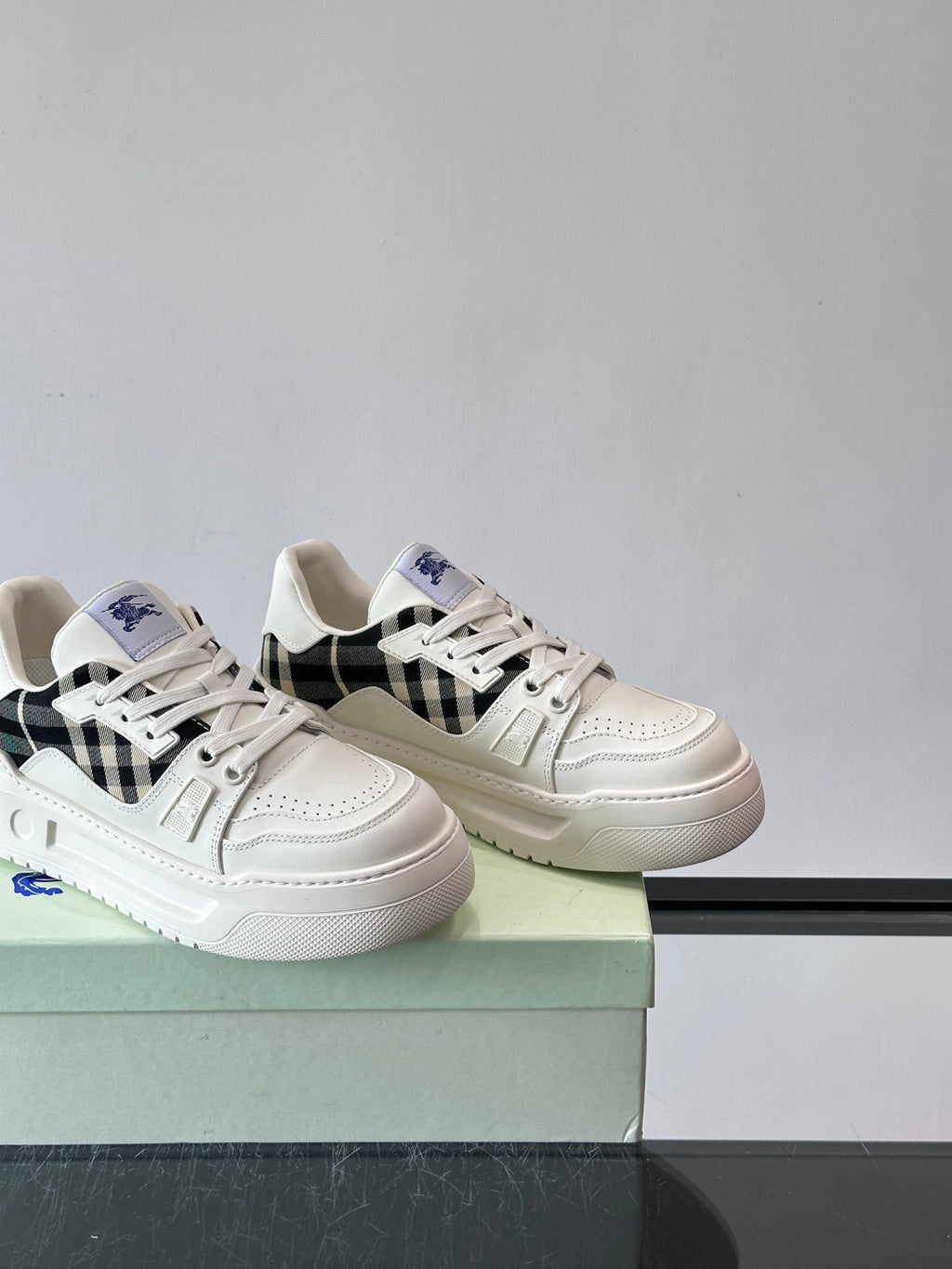 White lace-up sneakers with black check accents and blue logo, side view on box