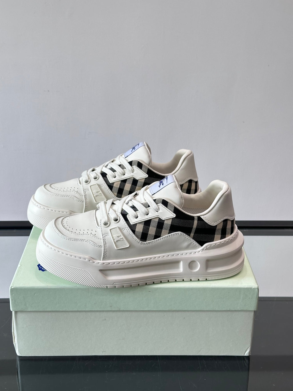 White lace-up sneakers with black plaid side insert and blue emblem on tongue