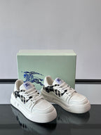 White lace-up sneakers on display box, black plaid details and blue logo