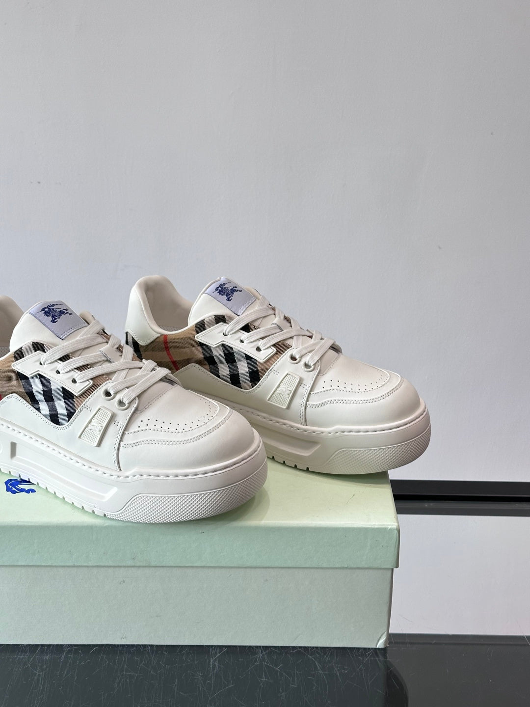 Two white sneakers on box with black-and-brown plaid side panel and blue logo