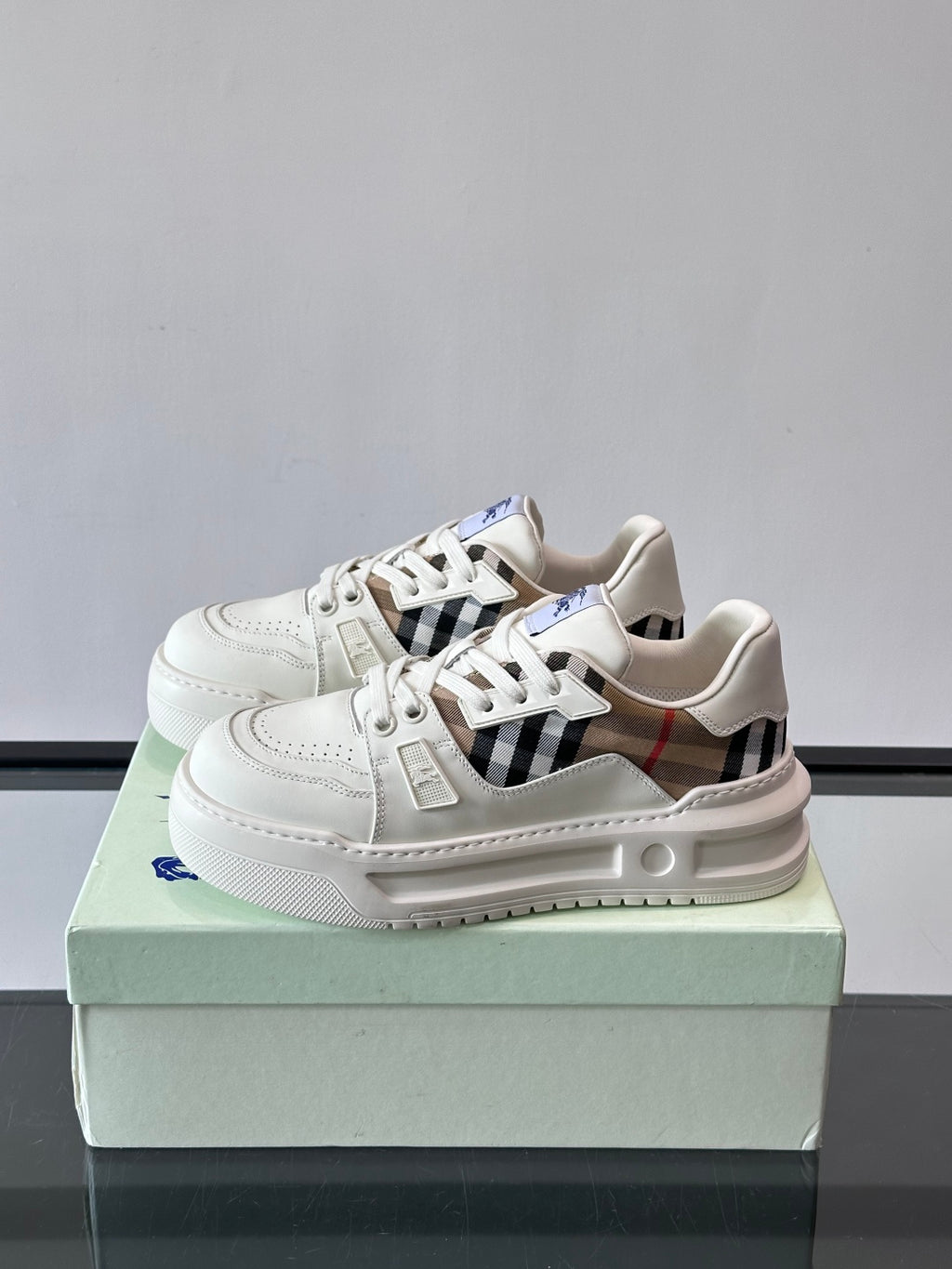 White lace-up sneakers on box with plaid strap detail and blue logo accent
