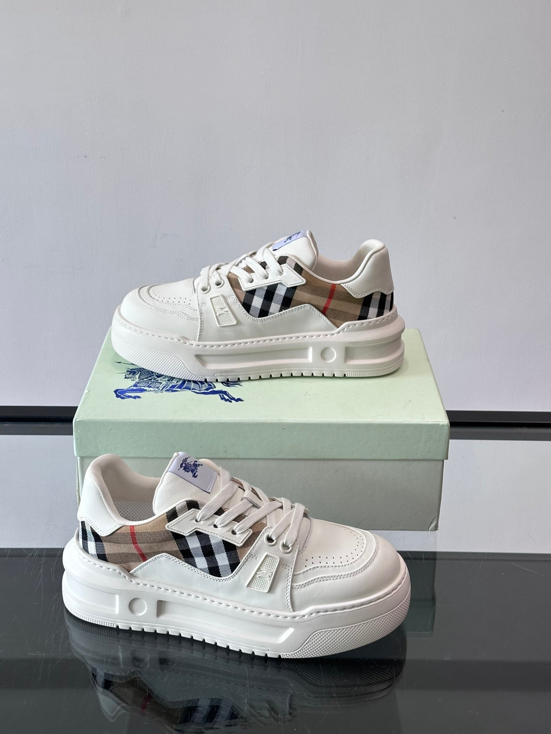 White low-top sneakers with blue logo, plaid strap, and thick rubber sole