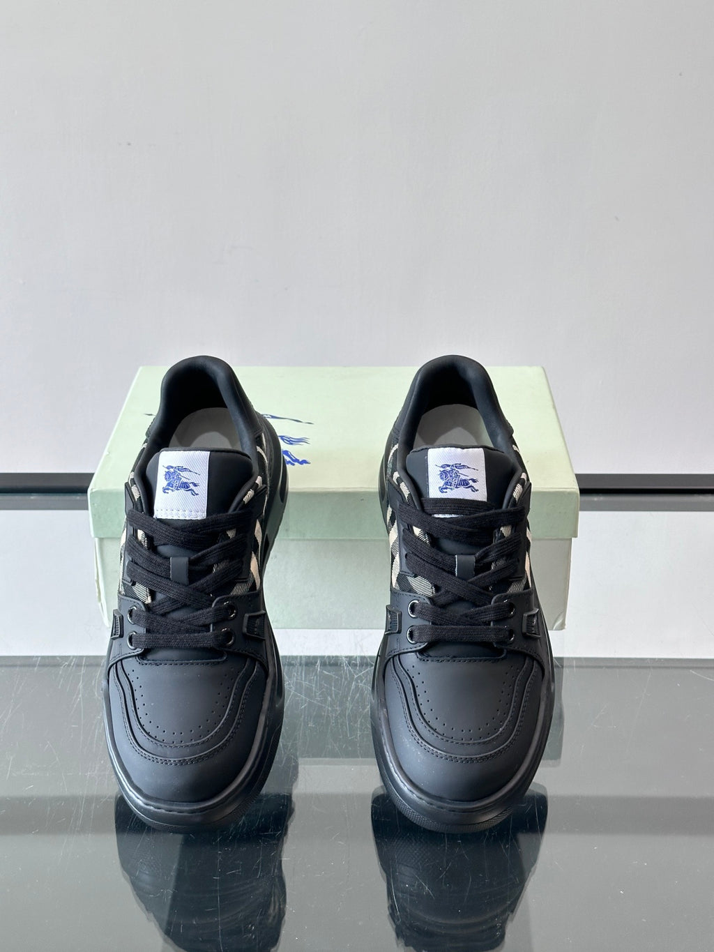 Front view of black lace-up sneakers with check panel detail and logo tag