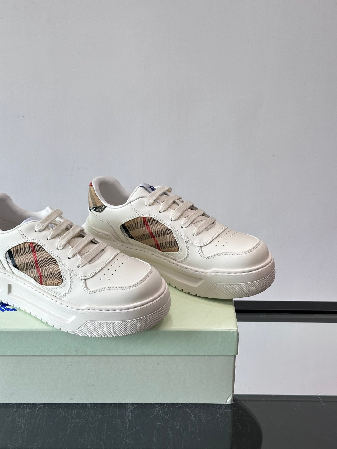 Two white sneakers on box, showing plaid side cutout and lace-up vamp