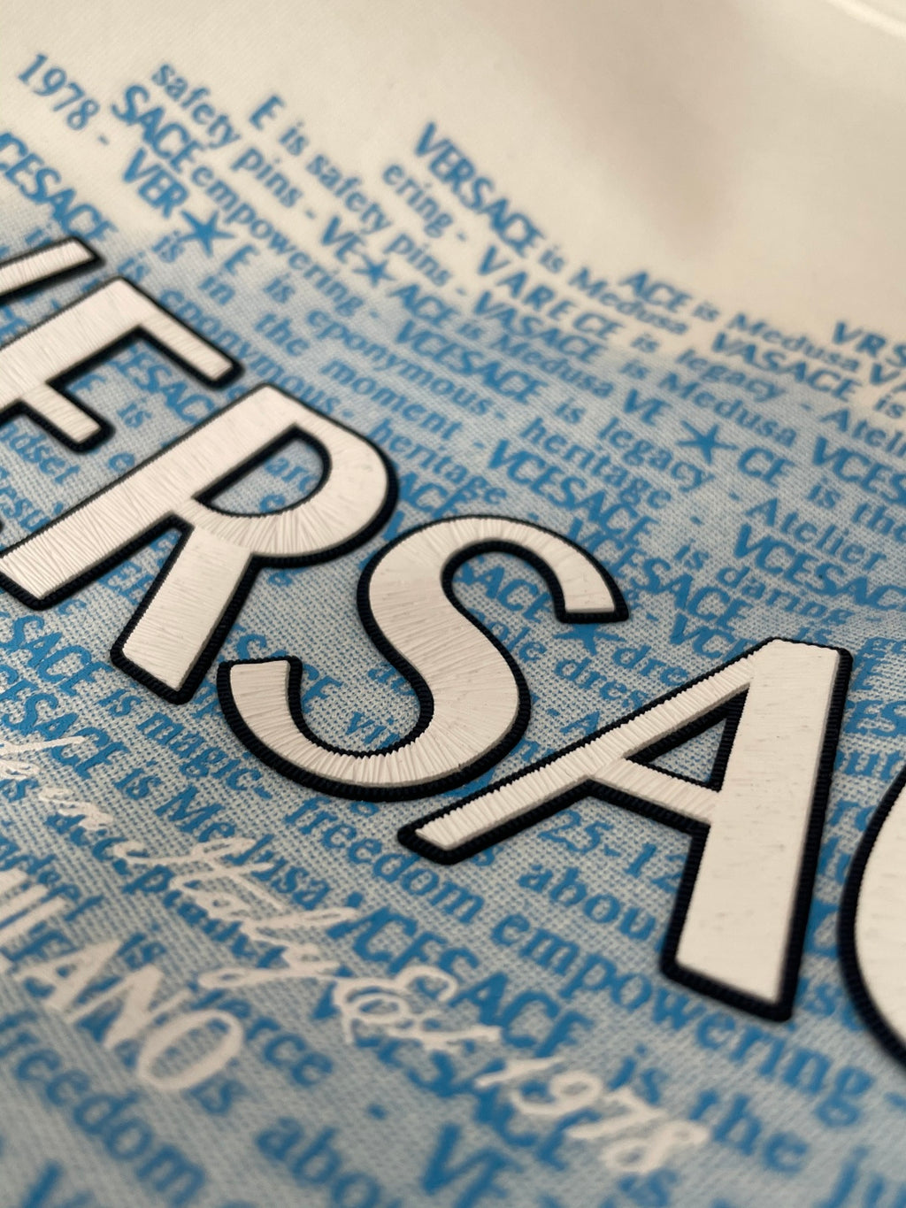 White sweatshirt featuring blue text pattern and large 'VERSACE' print