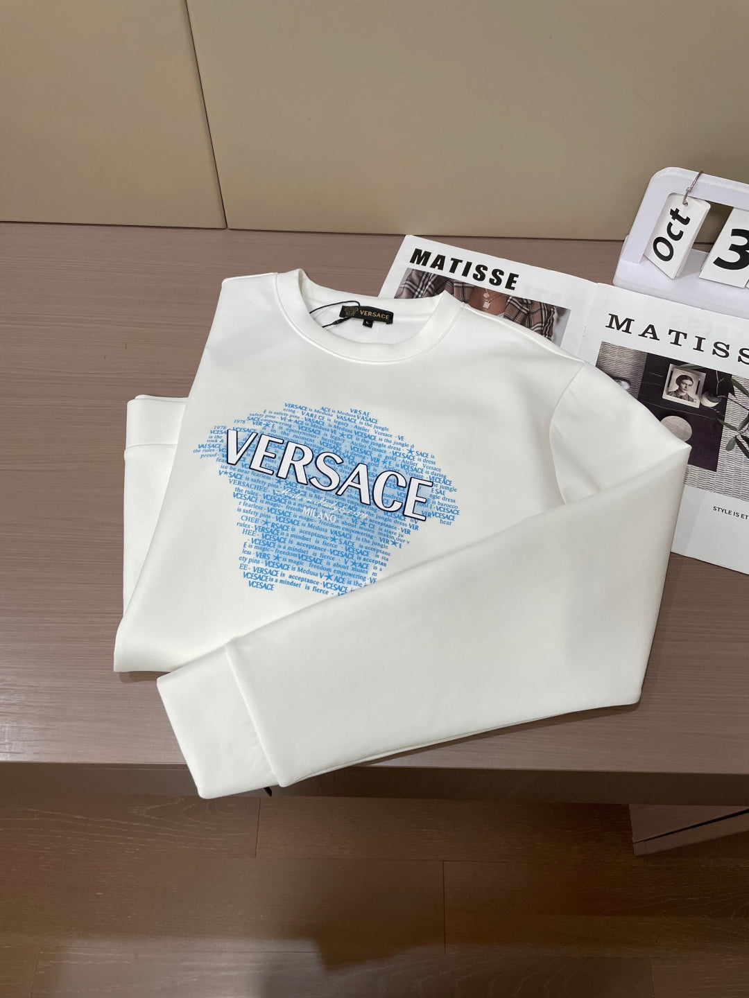 Folded white crewneck sweatshirt with blue Versace graphic front