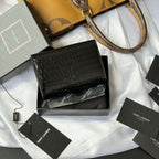 Black small leather bag with croc texture and flap closure, displayed on box