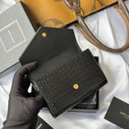 Black small bag with croc texture and gold snap, held in gloved hand