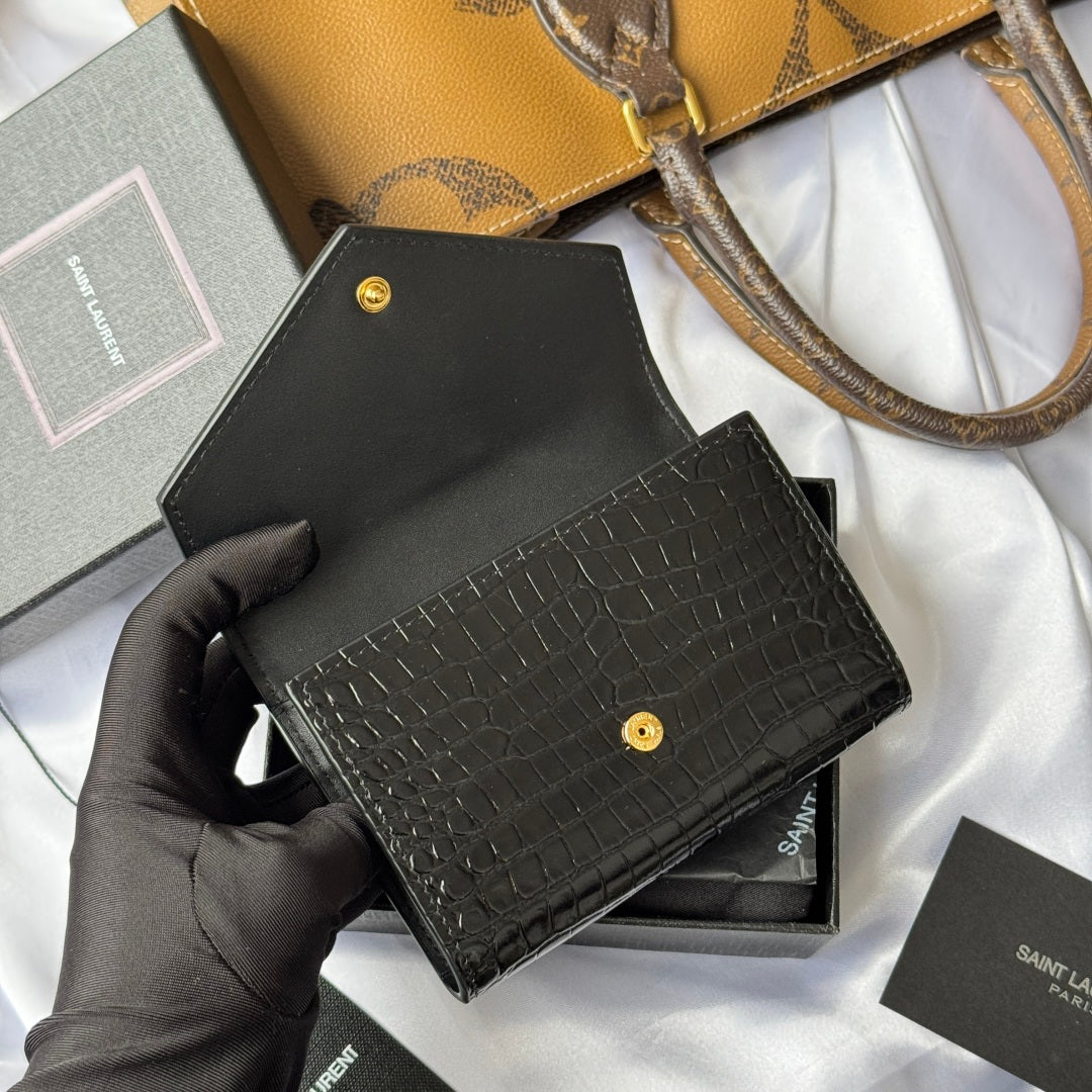 Black small bag with croc texture and gold snap, held in gloved hand