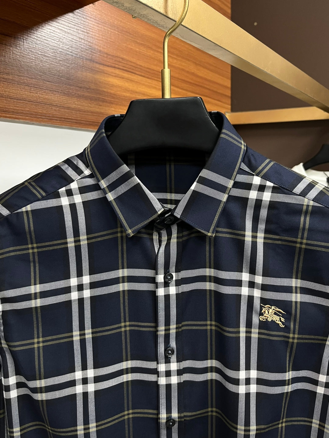 Navy plaid button-up shirt with pointed collar and small gold chest emblem