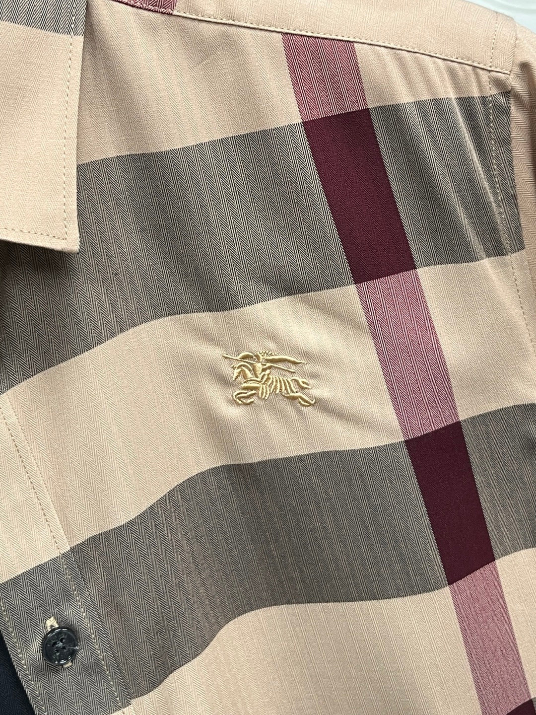 Burberry plaid long-sleeve shirt fabric close-up with gold crest emblem and buttons