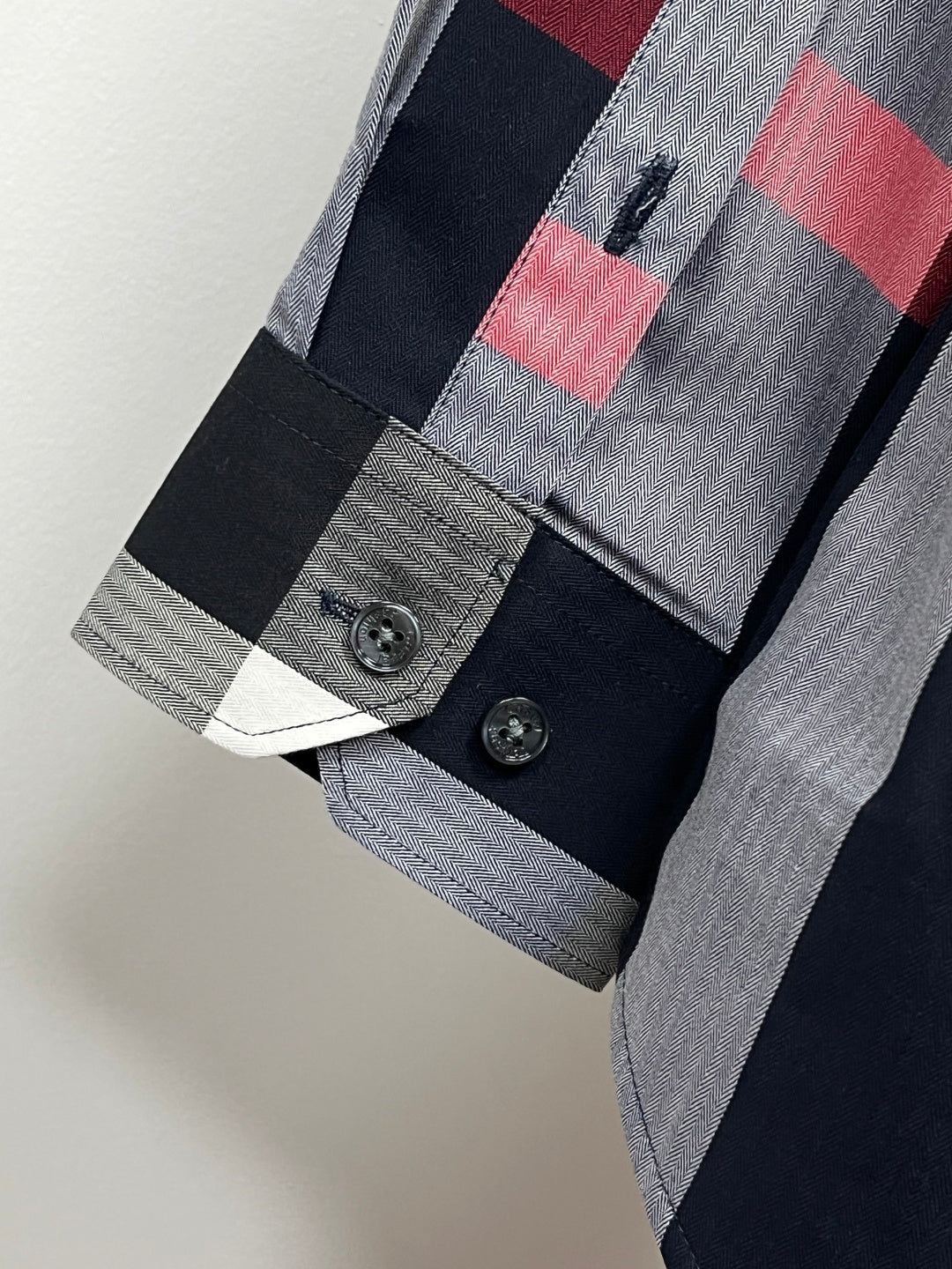 Long-sleeve plaid shirt cuff with dark buttons, navy and gray checks, red accent stripe