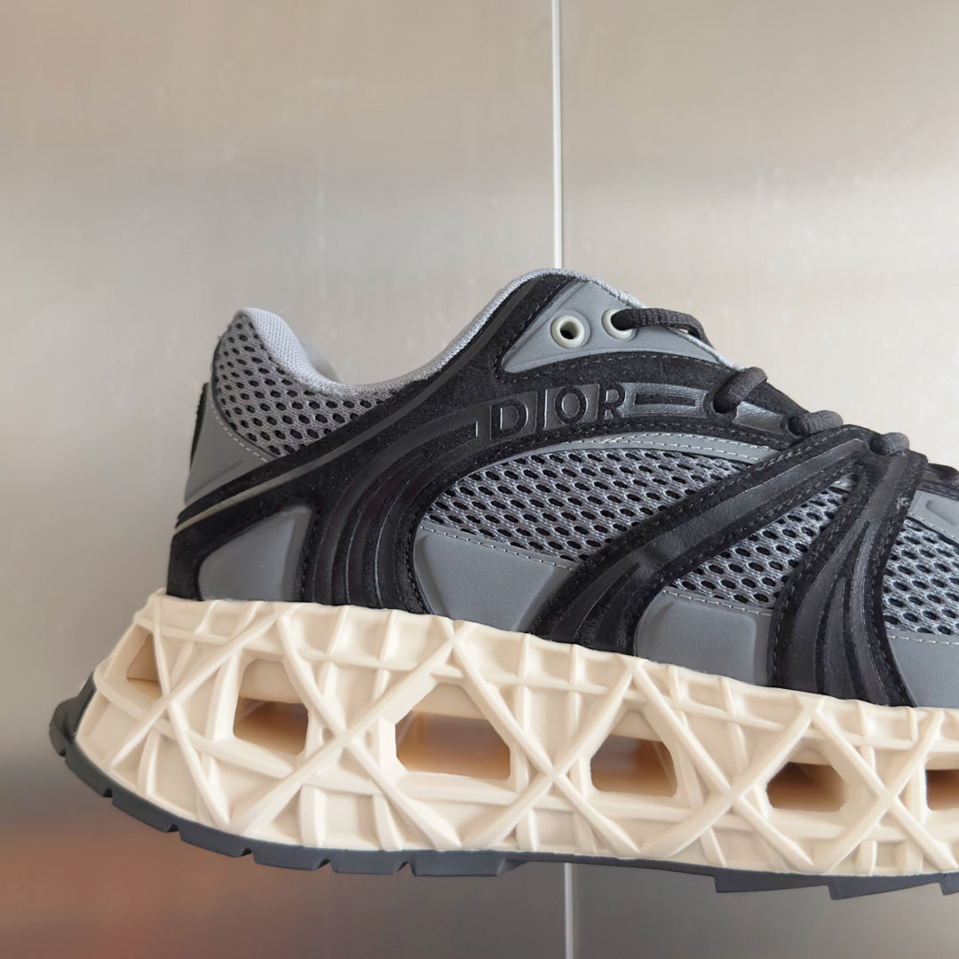 Dior unisex sneaker close-up, dark gray mesh with black logo panel and cream tread sole