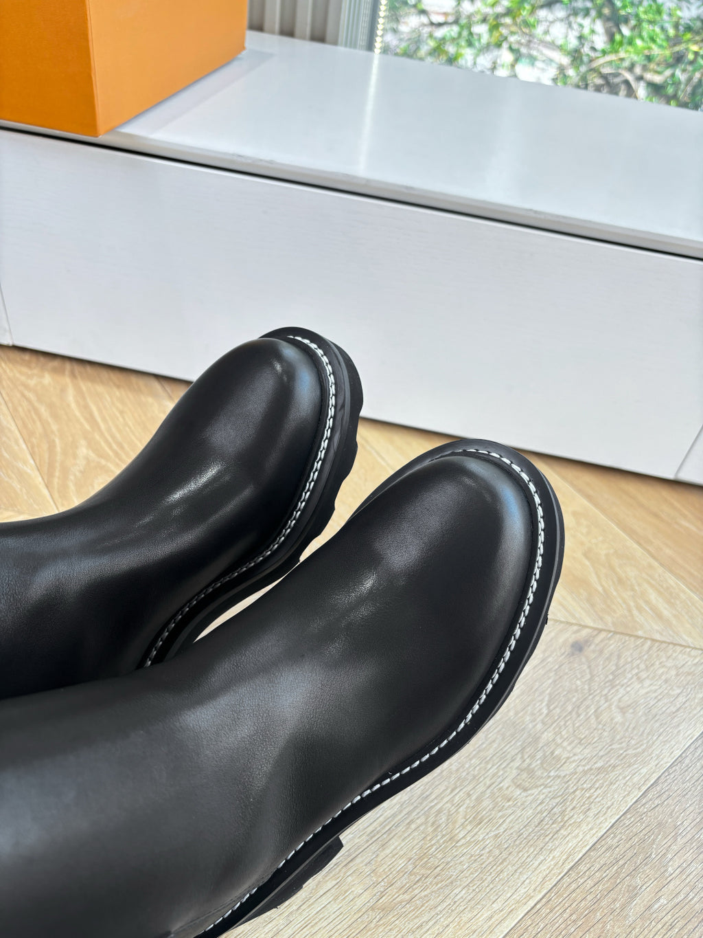 Black leather knee-high boots with contrast edge stitching, close-up